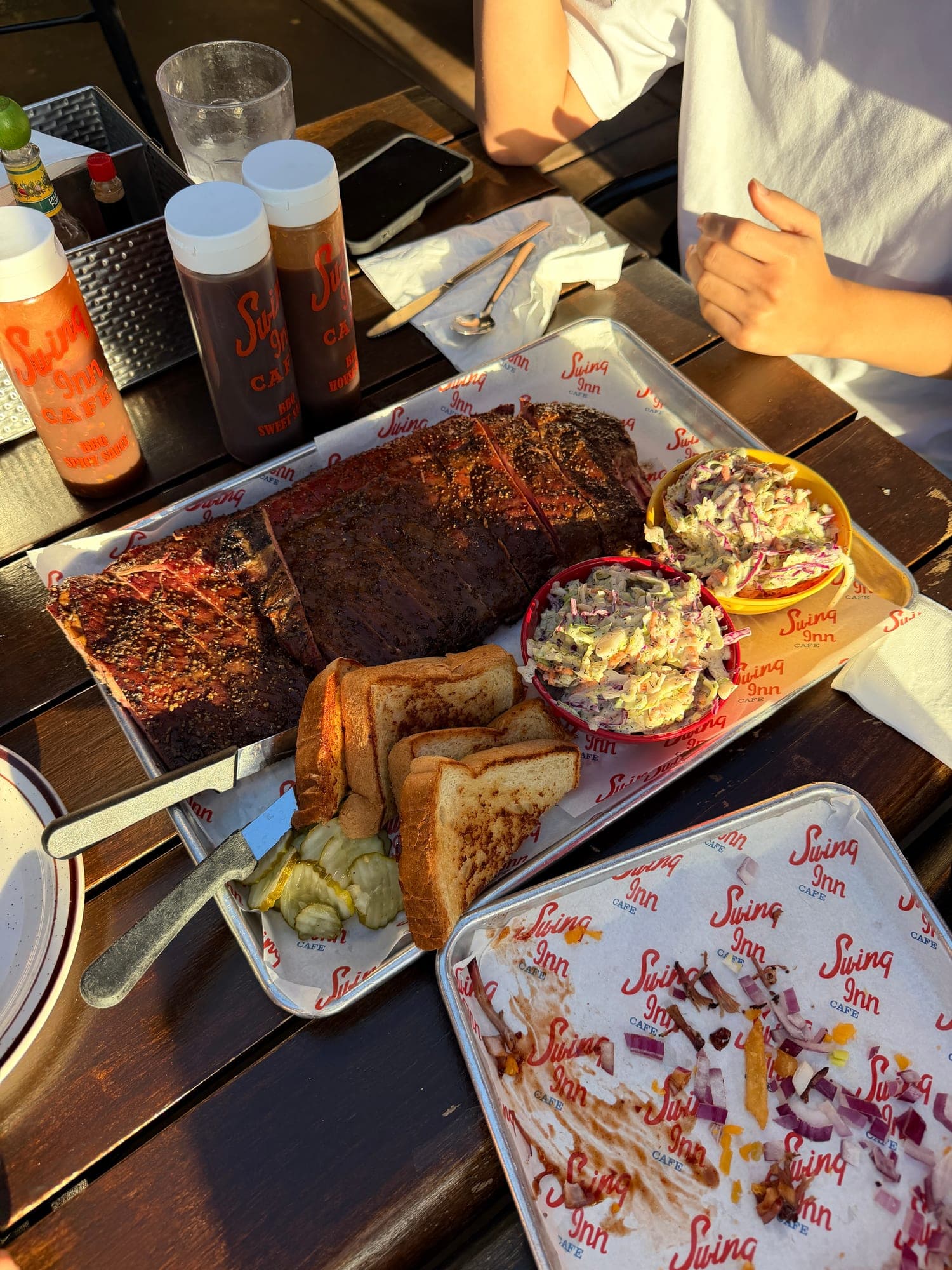 A tray of smoked brisket, ribs, coleslaw and toast with sauce bottles on a picnic table