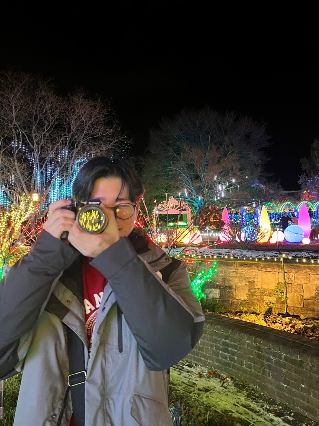 Ryan taking a photo with a Sony camera in front of a garden lit up with holiday lights at night